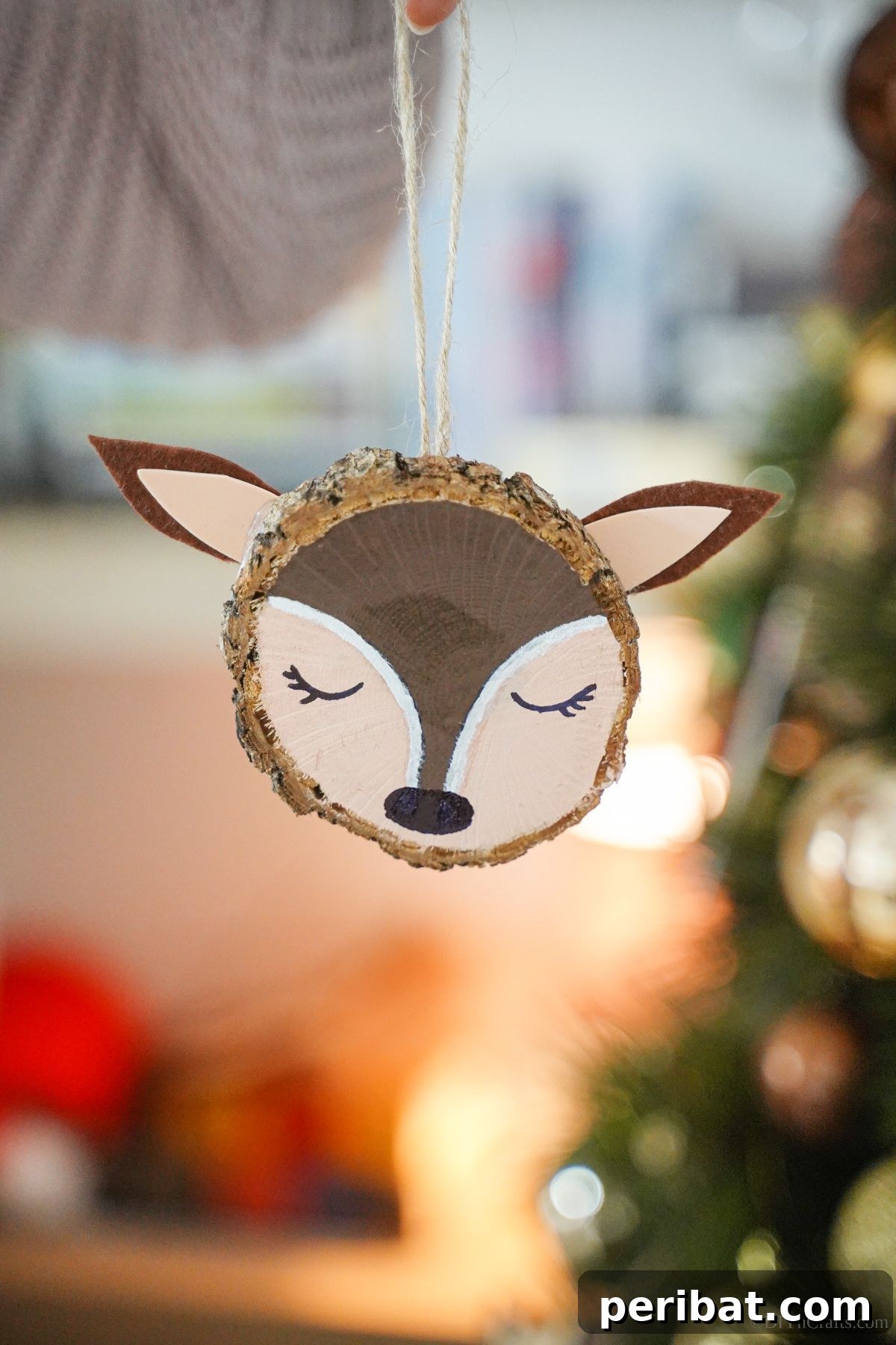 Naturally Charming Reindeer Wood Slice Decor 2 Painted wood slice reindeer ornament held against a festive Christmas tree