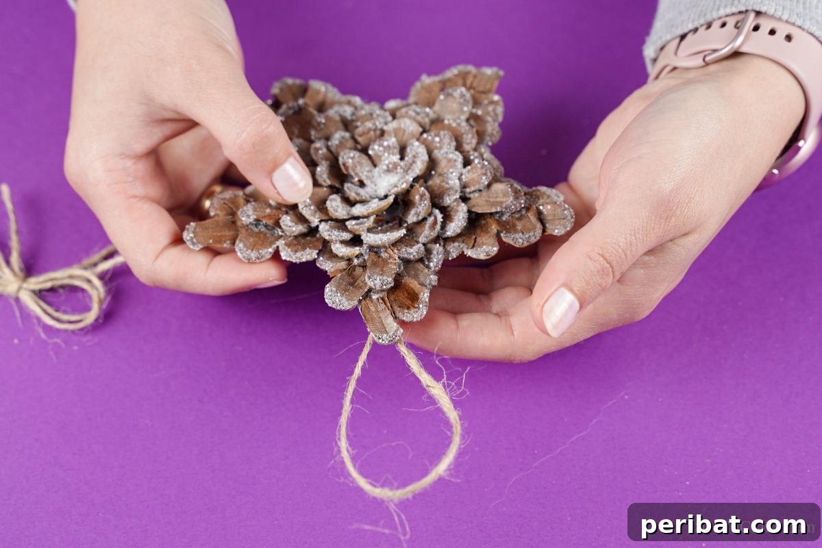 hand holding pinecone star with twine loop on back