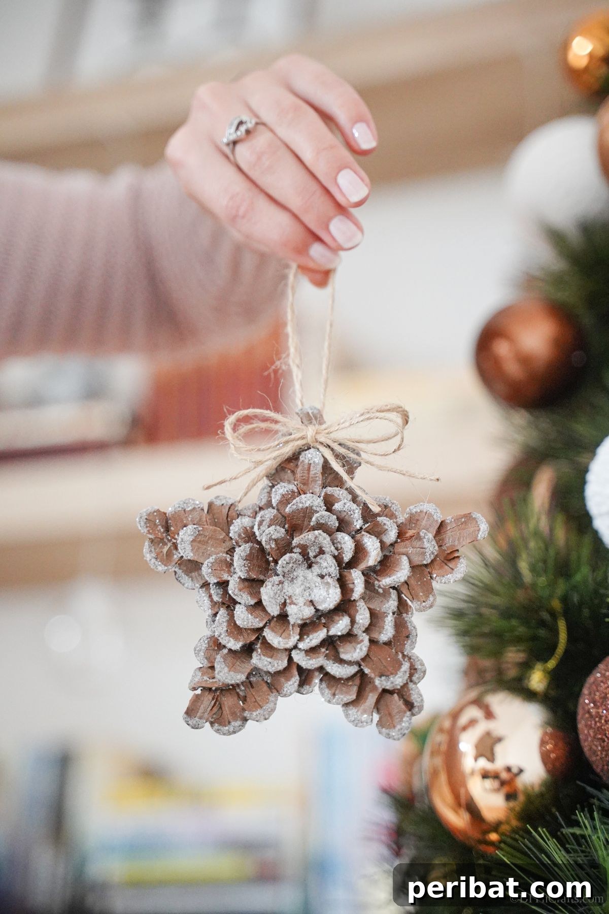 hand holding glitter pinecone star in front of holiday tree