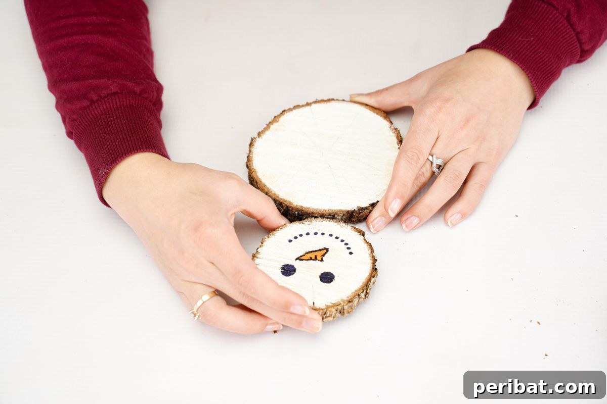 DIY Rustic Wood Slice Snowman Decor 10 Hands carefully holding together the small head wood slice and the medium body wood slice, secured with hot glue, forming the upper section of the snowman