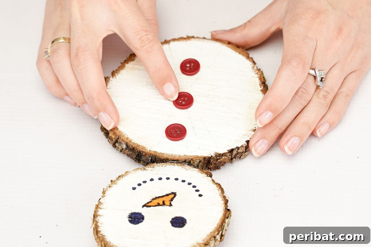 DIY Rustic Wood Slice Snowman Decor 11 A hand carefully gluing three red buttons in a vertical line down the middle of the snowman's body, adding classic detail to the wood slice craft