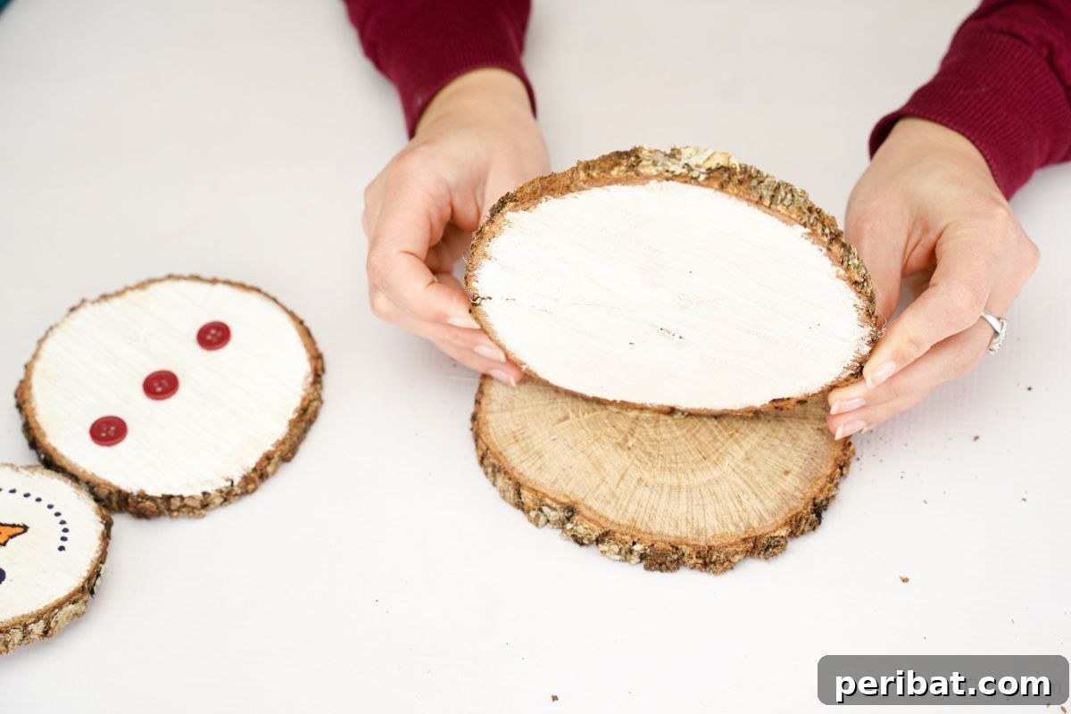 DIY Rustic Wood Slice Snowman Decor 12 A hand applying hot glue to the bottom edge of the largest wood slice (the snowman's base body) before securing it upright onto a flat wood slice base