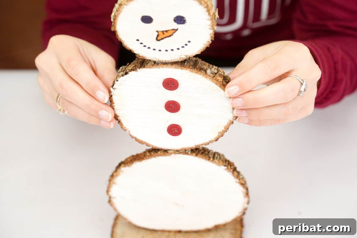 DIY Rustic Wood Slice Snowman Decor 13 Hands carefully holding the stacked painted wood slices together, forming the complete body of the snowman, ensuring secure attachment