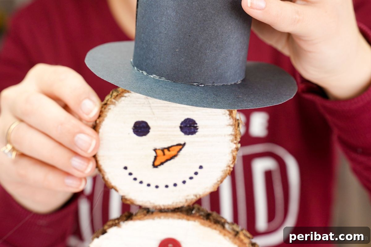 DIY Rustic Wood Slice Snowman Decor 14 A hand gently positioning the paper hat onto the head of the wood slice snowman, preparing to secure it with hot glue