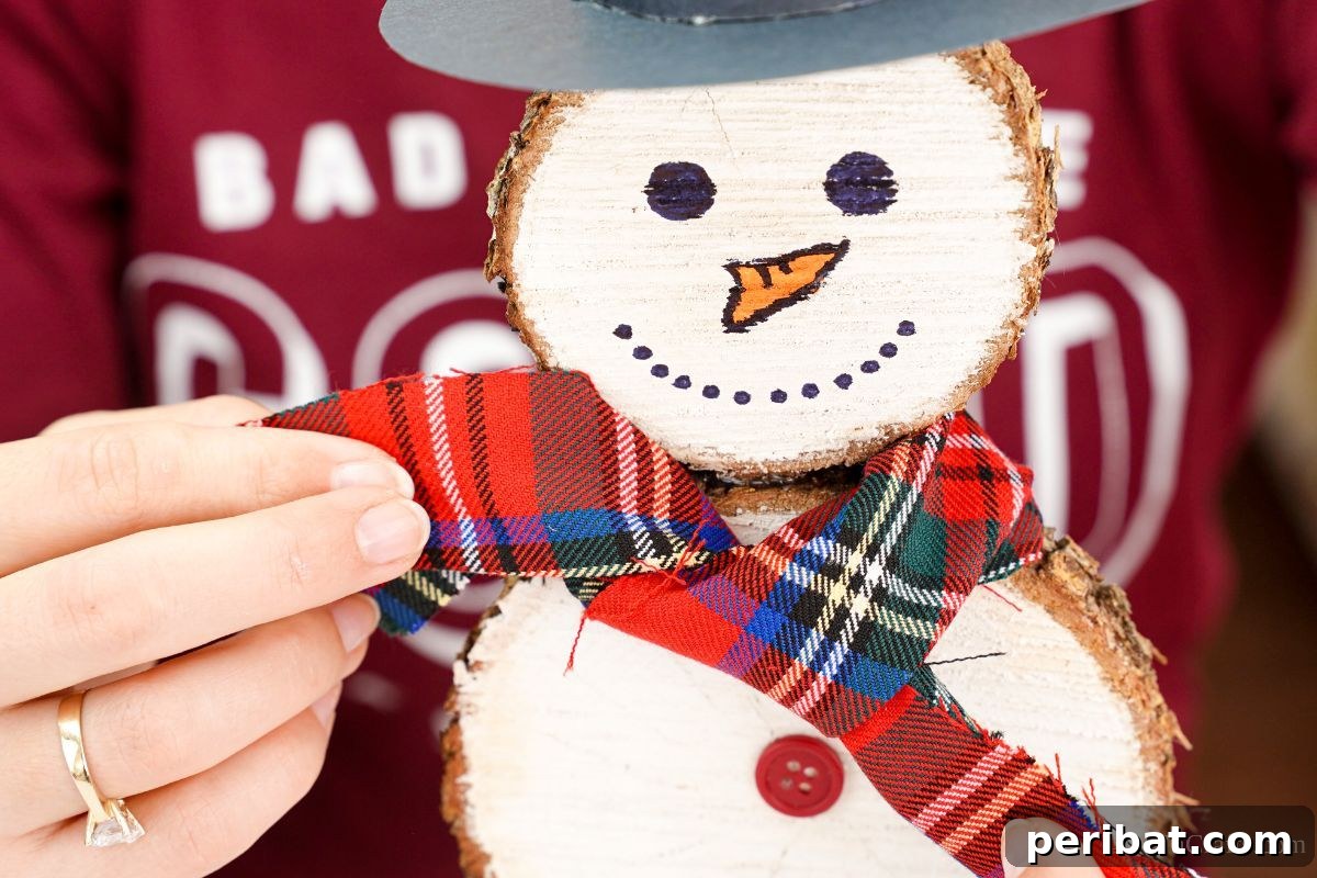 DIY Rustic Wood Slice Snowman Decor 15 A hand carefully draping a piece of plaid fabric around the neck of the wood slice snowman to create a rustic scarf