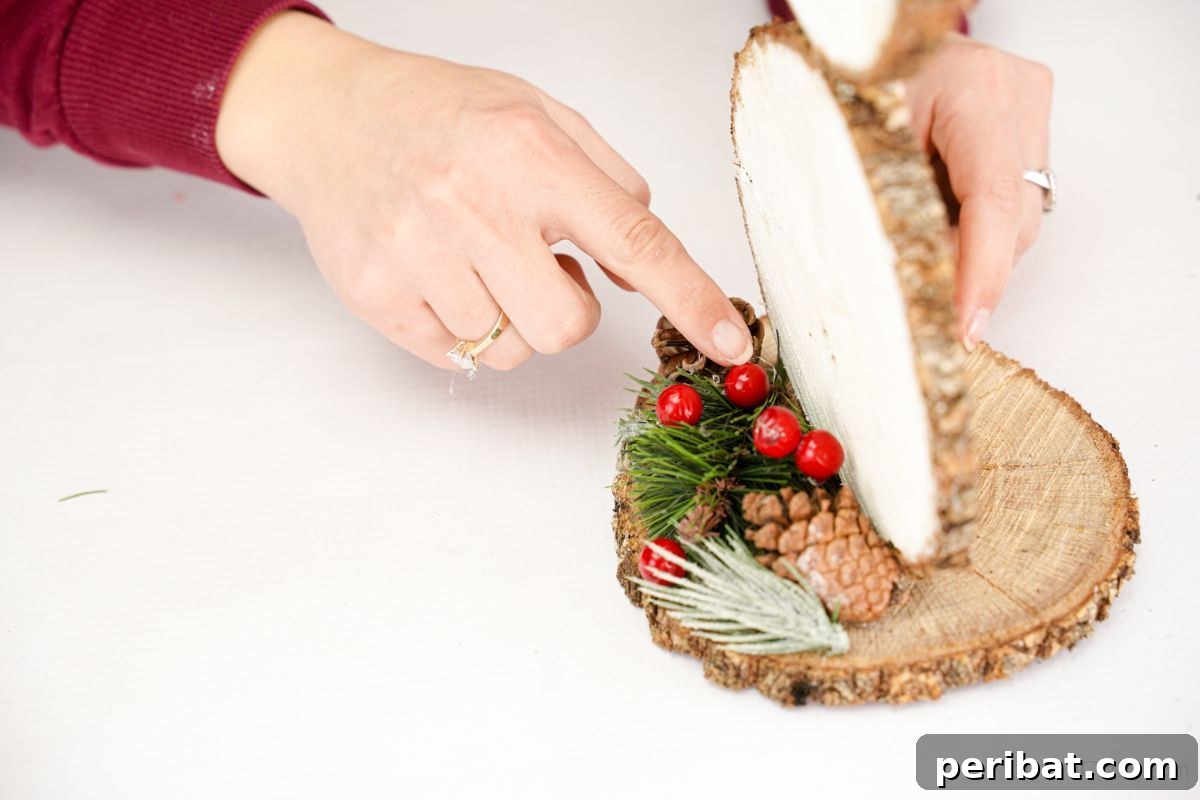 DIY Rustic Wood Slice Snowman Decor 16 Red berries and small green sprigs being carefully glued onto the base of the wood slice snowman, adding festive natural embellishments