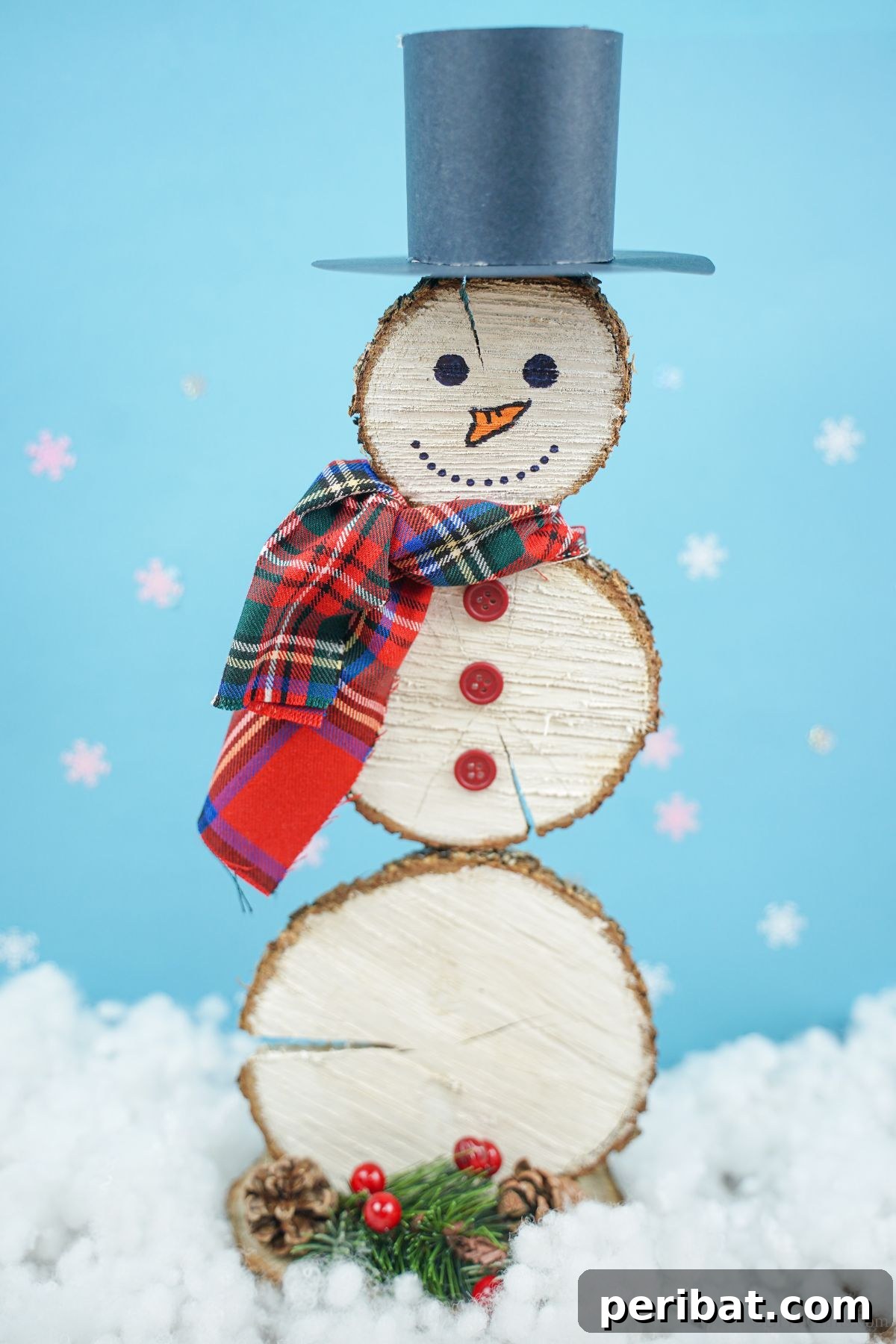 DIY Rustic Wood Slice Snowman Decor 22 Completed wood slice snowman in front of a light blue background with faux snow, highlighting its rustic charm and simplicity
