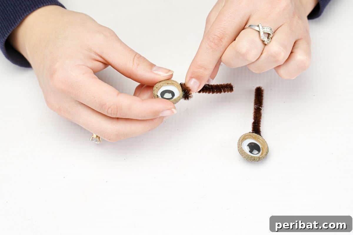 Hand gluing a pipe cleaner to an acorn top eye, demonstrating step 7 of the craft.
