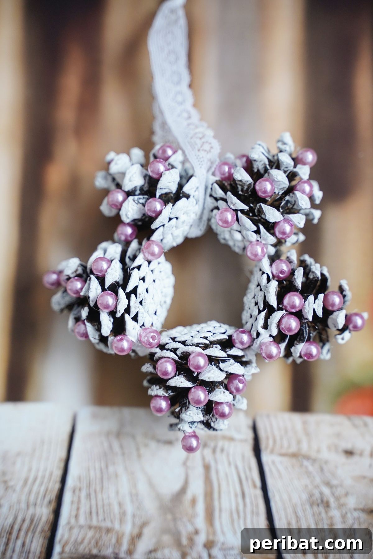 Glistening Bead-Adorned Pinecone Star 4 pinecone ornament in shape of star propped against fake wood background