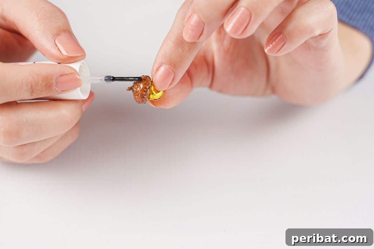 A person meticulously paints an acorn cap with clear fingernail polish, adding a glossy finish to the natural surface