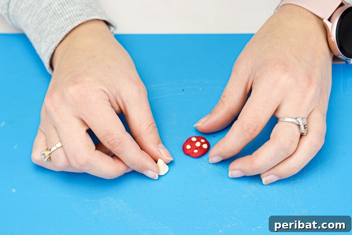 A hand expertly molds a piece of white clay into a cylindrical shape, forming the base or stalk of a miniature mushroom, showcasing the crafting process for the ornament.