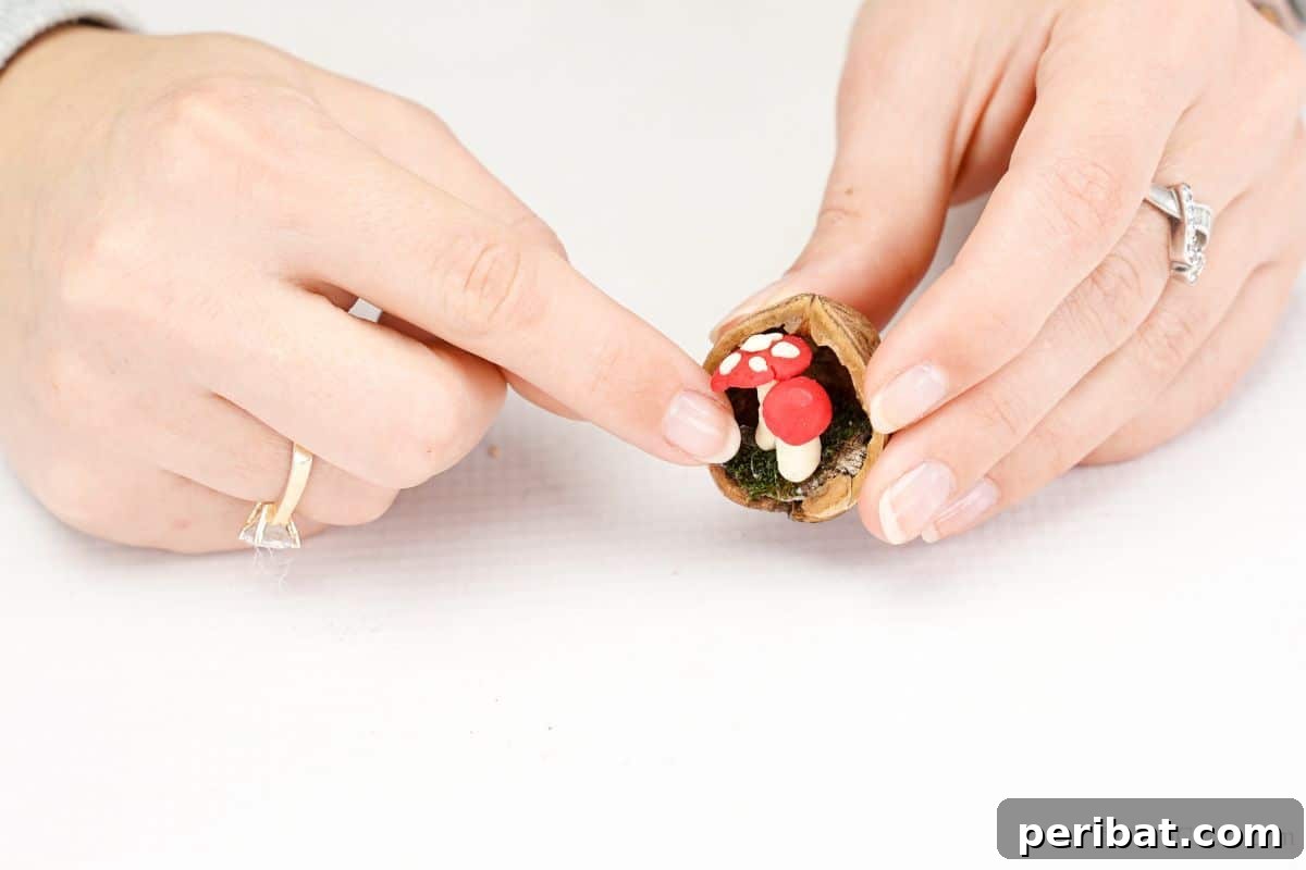A finger carefully places a miniature mushroom inside a walnut shell, demonstrating the final step in assembling the ornament's inner scene.