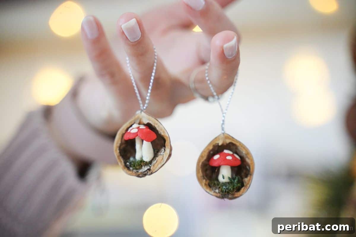A hand gracefully holds two completed walnut shell ornaments, suspended by their strings, showcasing the delicate craftsmanship and the charm of the miniature world contained within each shell.