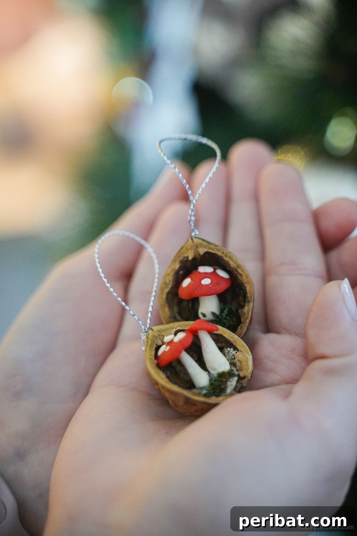 A pair of hands gently holds two miniature mushroom ornaments crafted within walnut shells, emphasizing the small scale and delicate nature of the DIY Christmas decorations.