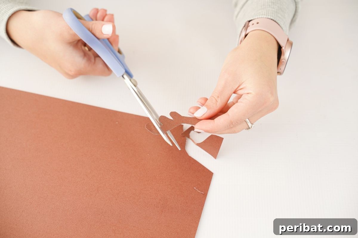 A hand meticulously cutting an antler shape out of brown paper, a key component for the egg carton reindeer craft.