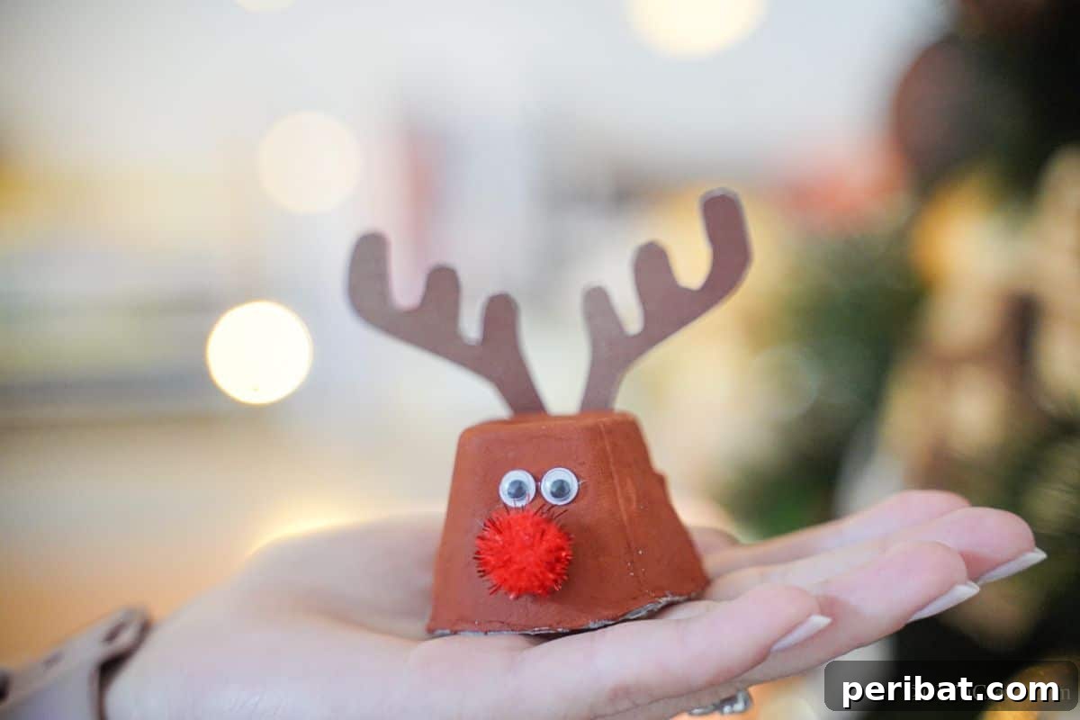 A child's hand gently holds an adorable egg carton reindeer, showcasing the simple charm of this DIY Christmas craft against a soft background.