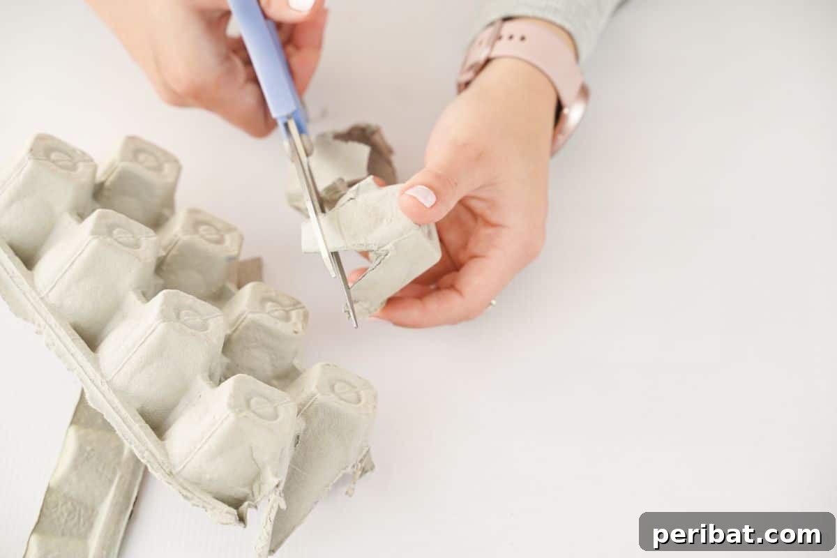 A blue scissor precisely cutting individual cups from an egg carton, demonstrating the first step in creating the reindeer craft.