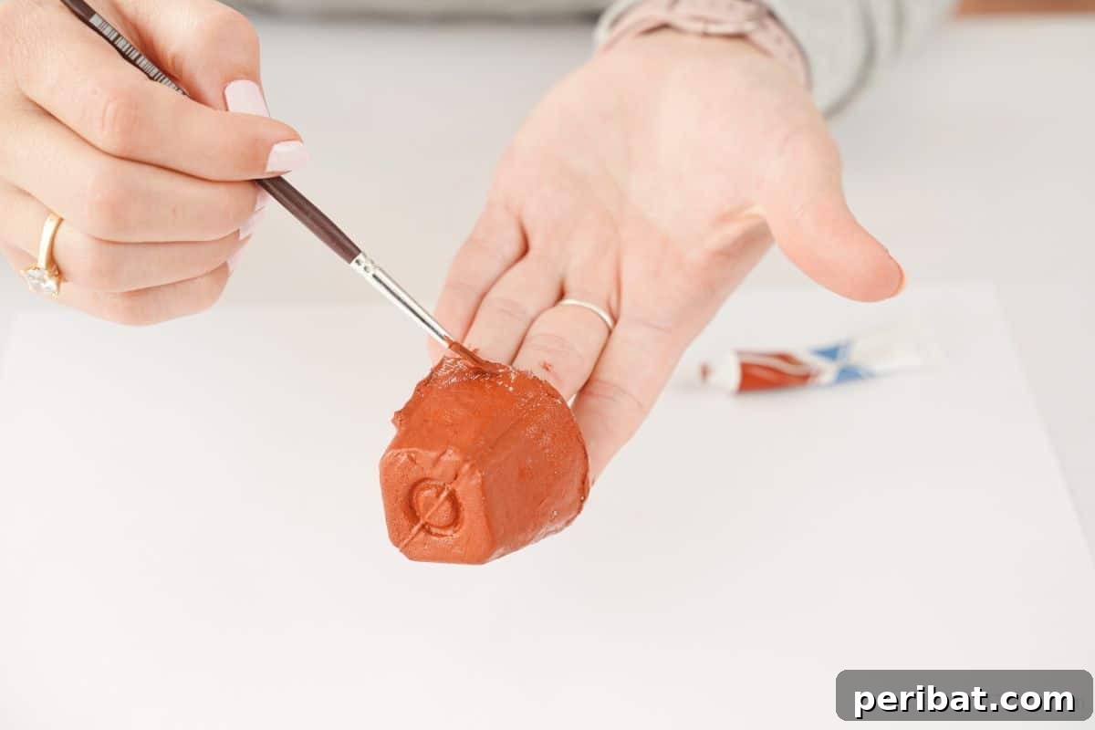 A hand carefully painting an egg carton cup brown, illustrating the coloring step for the reindeer craft.