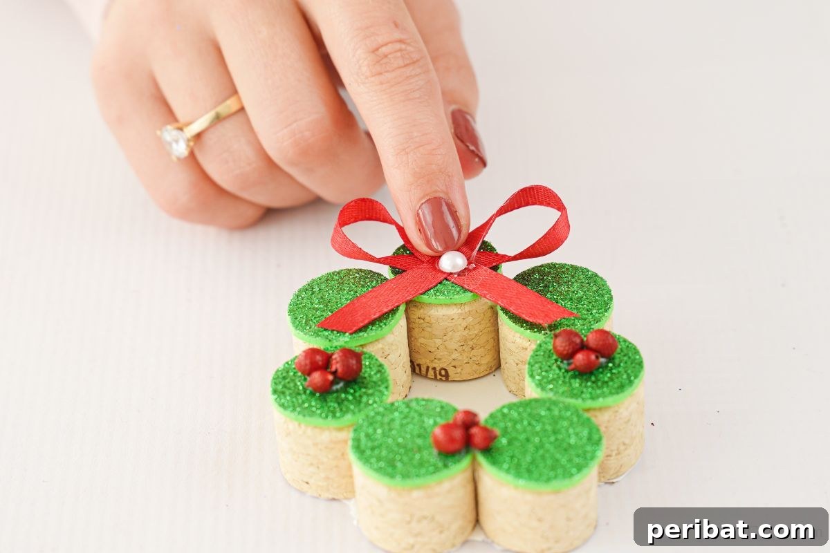 Repurposed Cork Wreath Charm 17 hand holding white bead on front of red bow on cork ornament