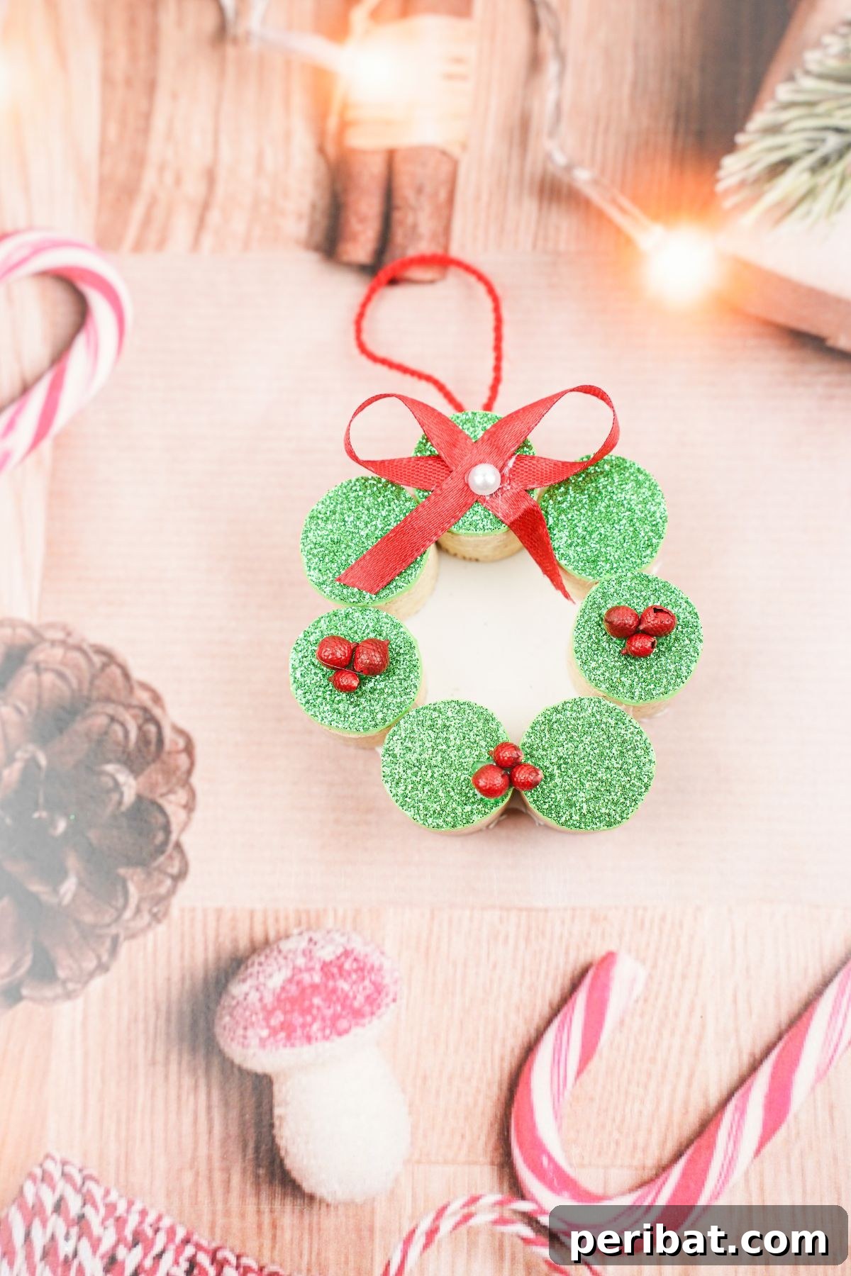 Repurposed Cork Wreath Charm 21 Wine cork wreath ornament with a red bow and green glitter, placed on paper with pinecone and peppermint designs