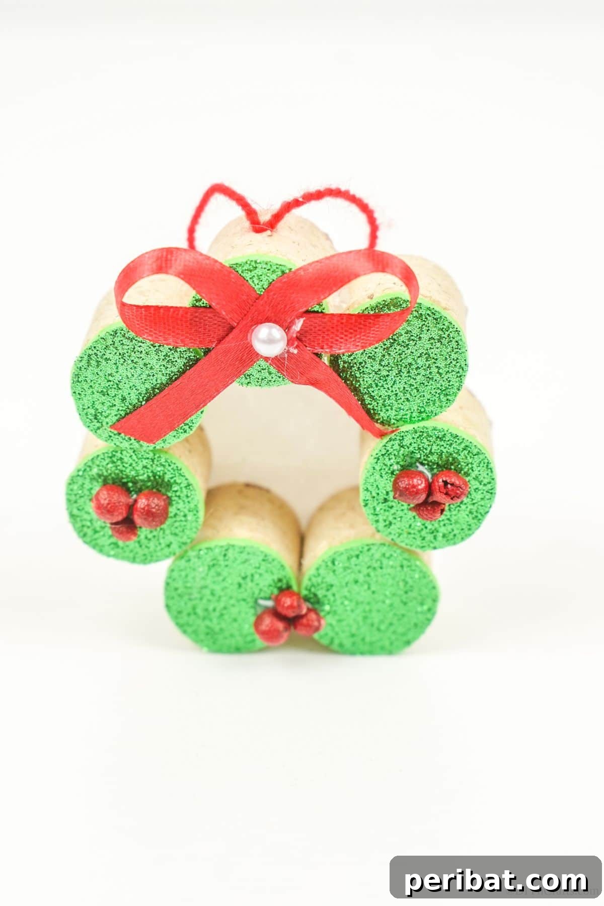 Repurposed Cork Wreath Charm 22 Close-up of a finished wine cork ornament with a red bow, sitting on a white table