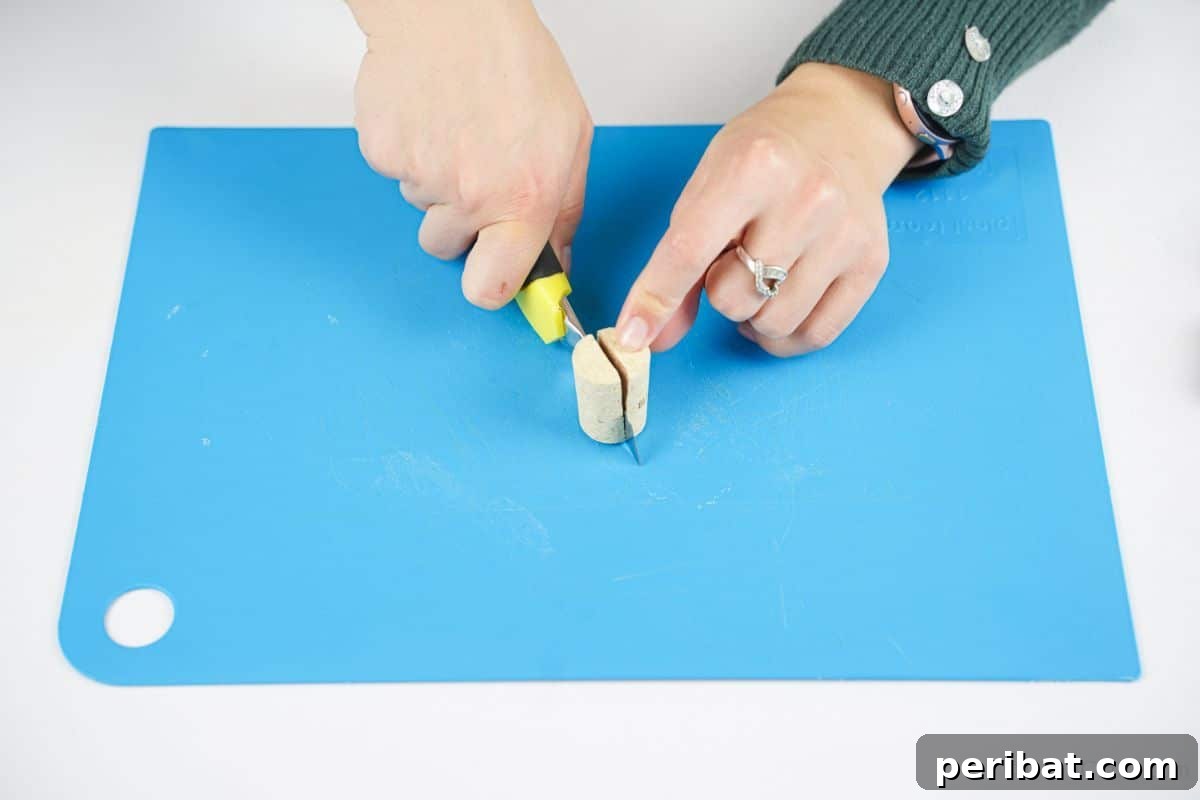Wine Cork Express Christmas Ornament 8 A yellow craft knife expertly used to cut a wine cork in half lengthwise on a blue mat, preparing it for assembly