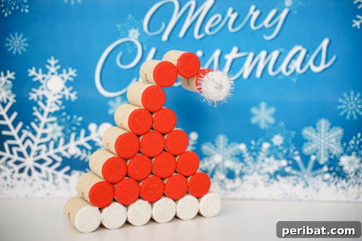A blue and white 'Merry Christmas' sign serves as a festive backdrop for a charming wine cork Santa Claus hat, displayed on a white table.
