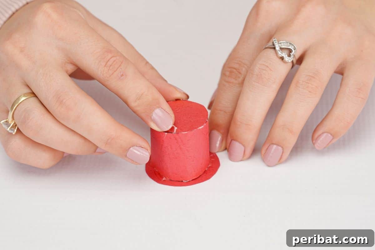 Woodland Pinecone Snowman Charm 9 hand holding top hat made of red paper on white table