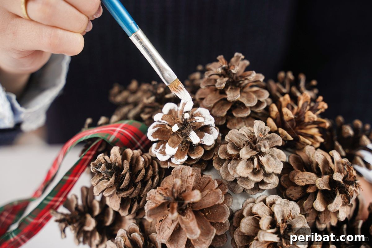 Festive Pinecone Ball Door Ornament 12 Blue paintbrush adding white paint onto the tips of pinecones, creating a snow-covered effect