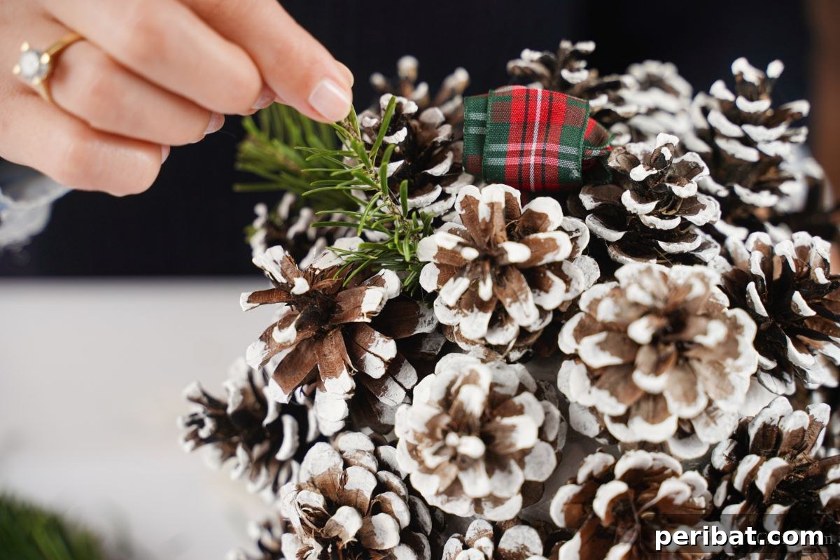 Festive Pinecone Ball Door Ornament 13 Hand adding fake greenery in between pinecones on the ball, enhancing its festive look