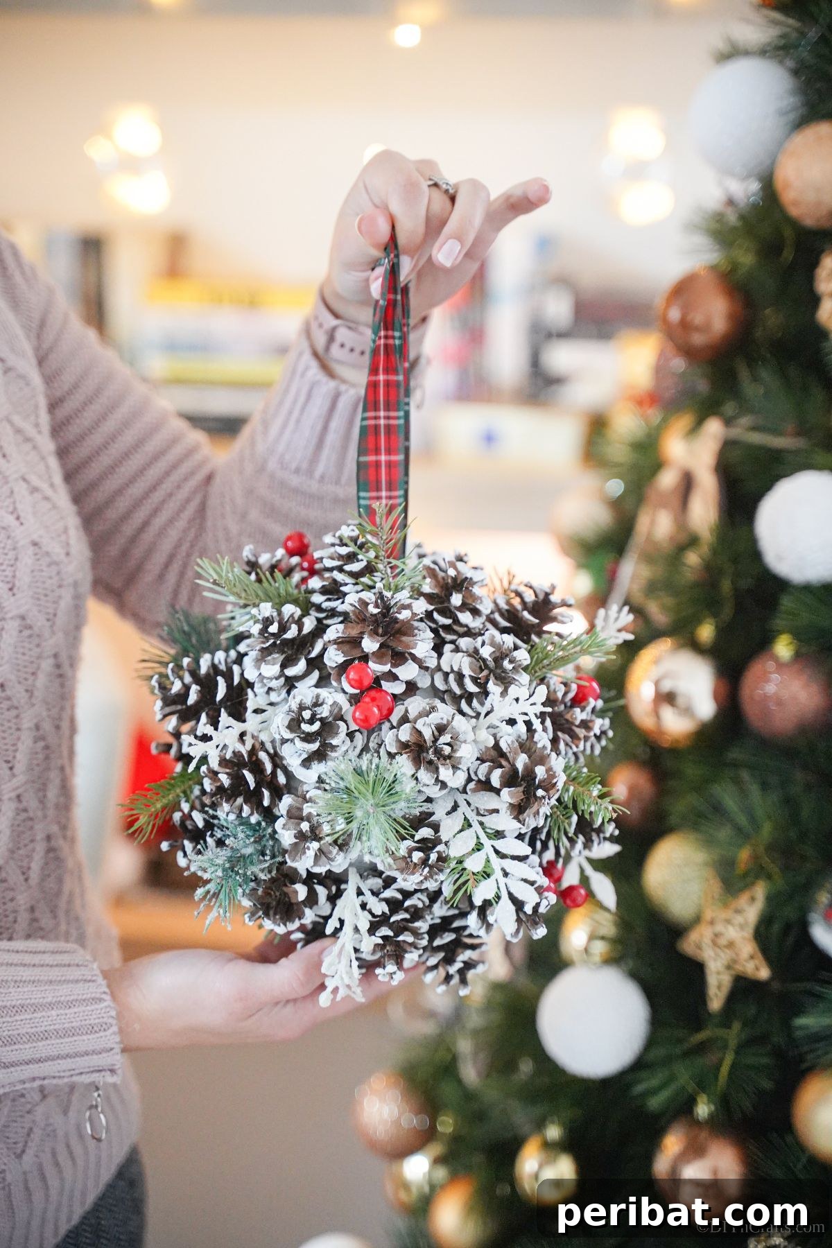 Festive Pinecone Ball Door Ornament 4 Woman in pink sweater holding pinecone door hanger in front of a Christmas tree, ready to decorate