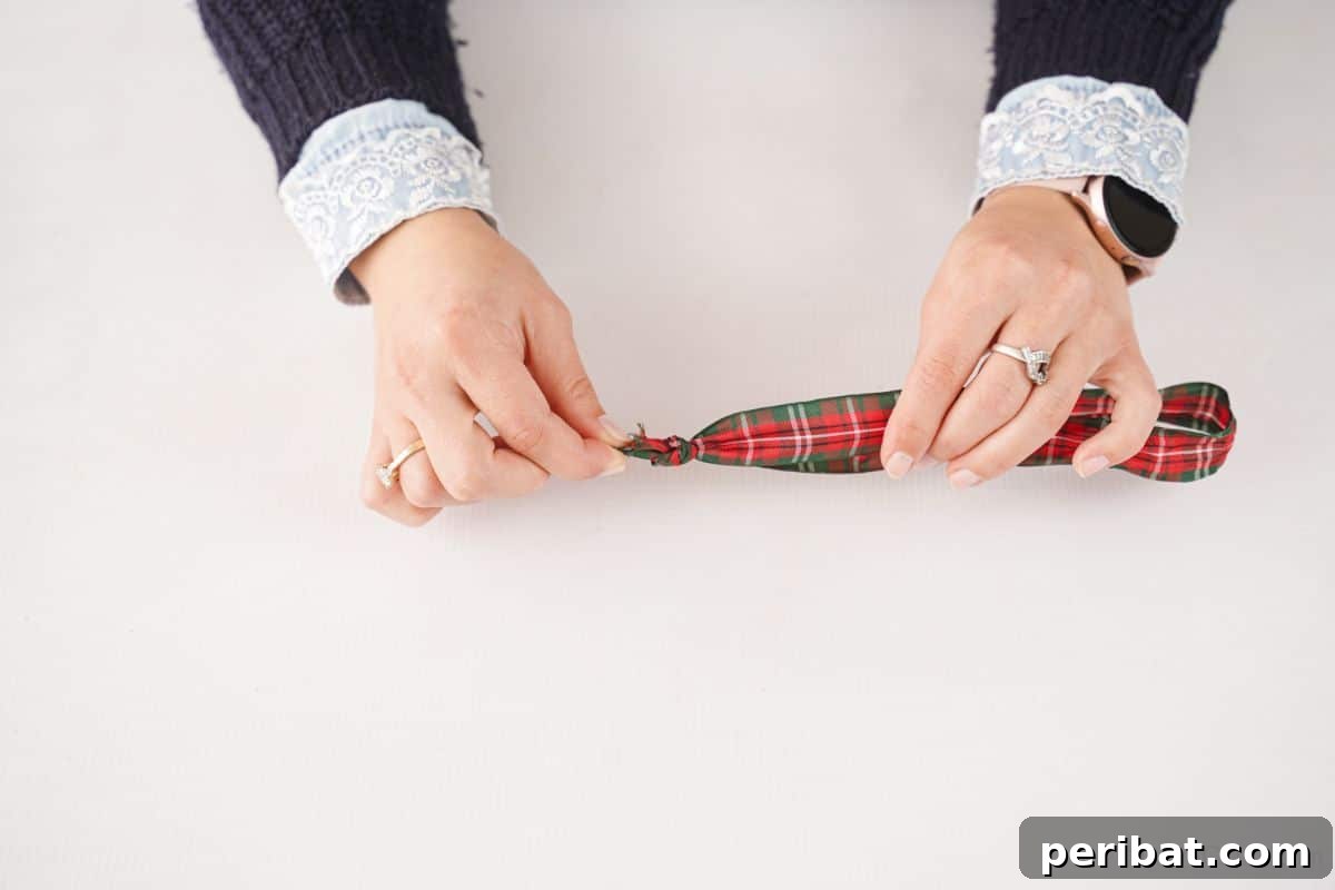 Festive Pinecone Ball Door Ornament 9 Hands tying a length of plaid ribbon into a loop, preparing for the door hanger