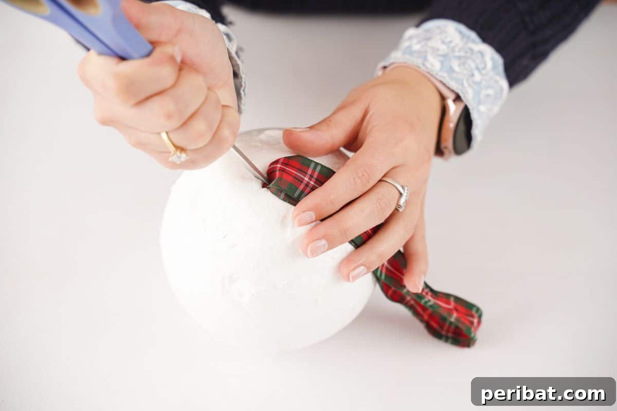 Festive Pinecone Ball Door Ornament 10 Using the end of scissors to poke the tied ribbon into the top of a styrofoam ball, securing the hanger