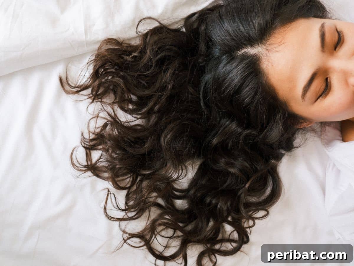 A woman lying on a comfortable bed, gently arranging her long hair to prevent damage, demonstrating careful hair handling.