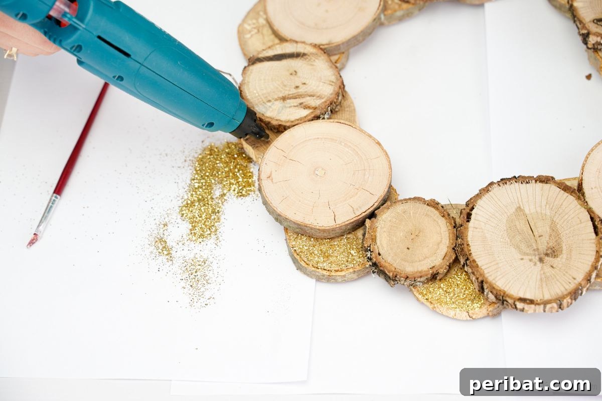Natural Branch Slice Wreath Adorned with Pinecones 12 Hot glue gun applying glue between wood slices, preparing for glitter