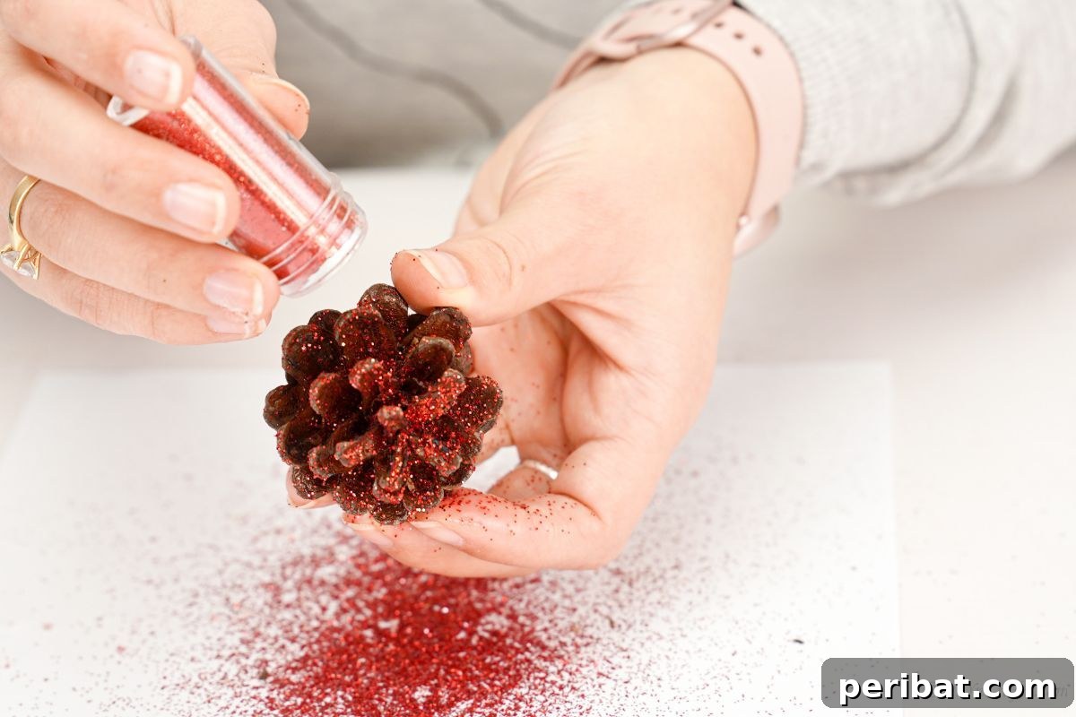 hand sprinkling glitter onto pinecone