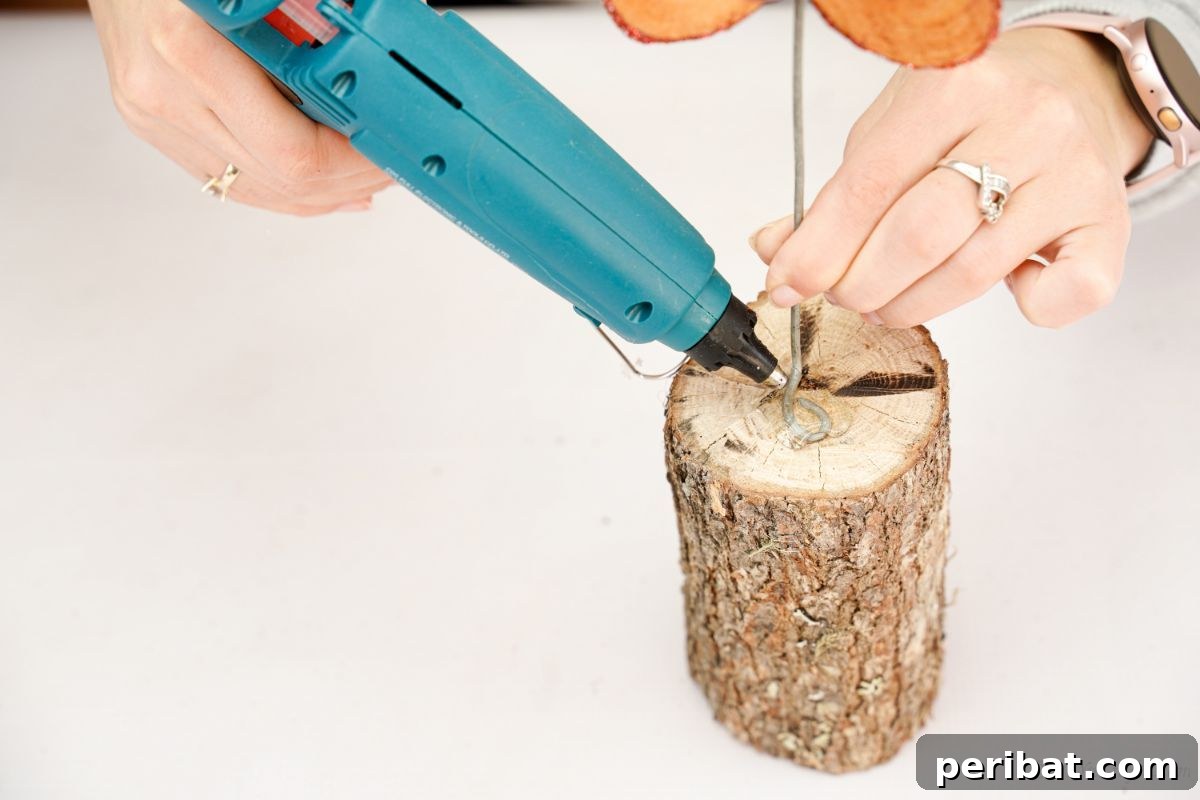blue glue gun gluing stem of wood slice flower onto log