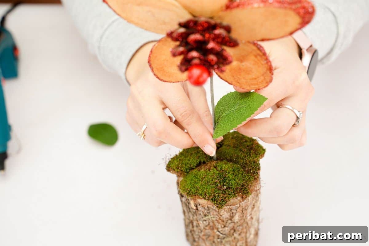 hand putting fake leaves on wood slice flower stem