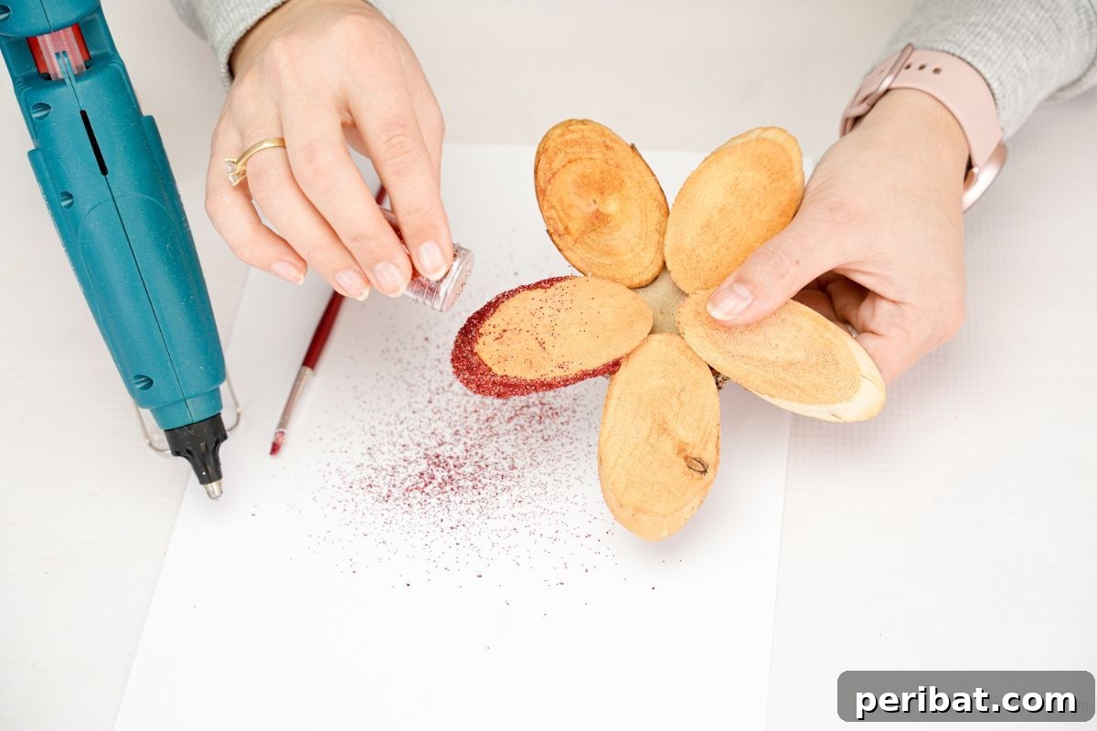 red glitter being sprinkled on edge of wood slice flower