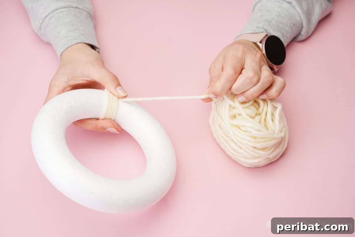 Whimsical Woolly Lamb Easter Wreath 8 Hand securing the beginning of cream yarn to a styrofoam wreath form, starting the wrapping process.