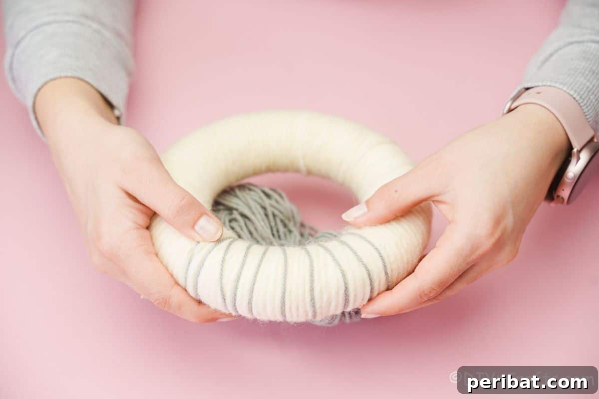 Whimsical Woolly Lamb Easter Wreath 10 Hands delicately wrapping grey accent yarn around a fluffy cream wreath, adding texture to the sheep's body.