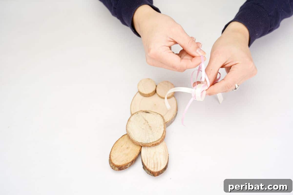 hand making pink bow above wood slice bunny
