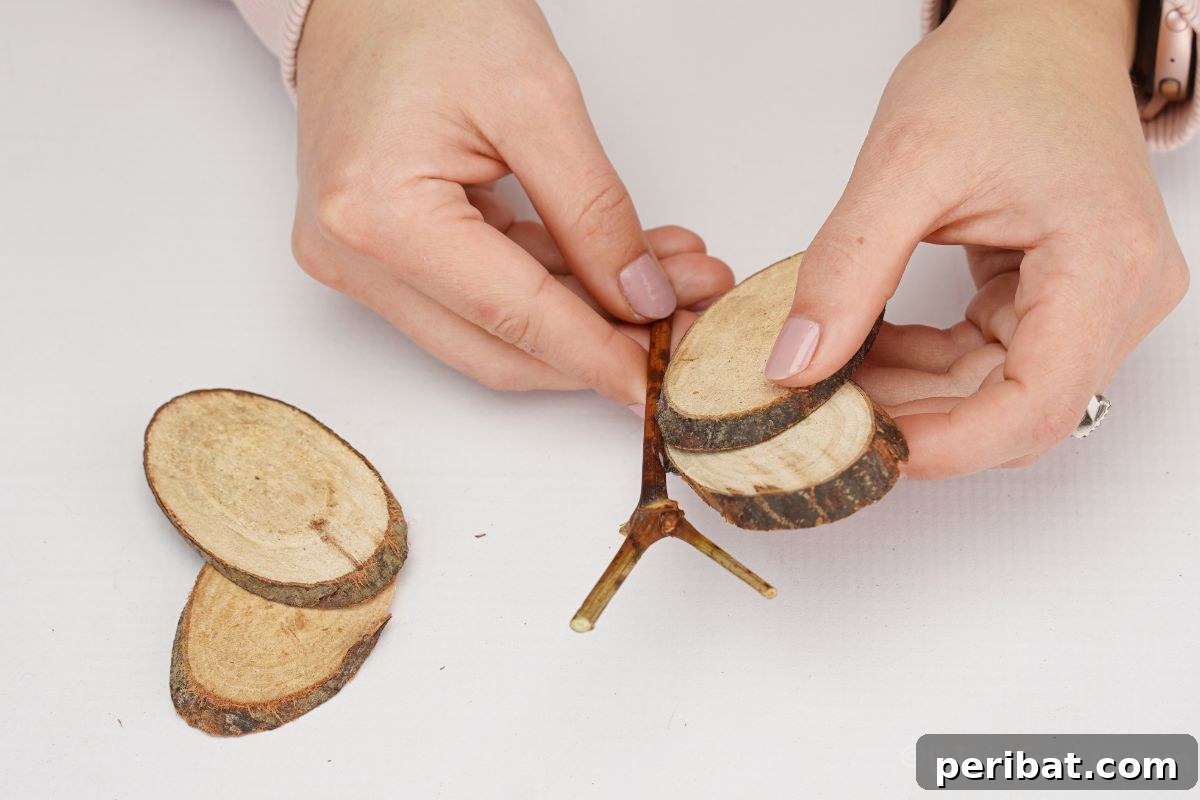 A hand applying hot glue to attach the wood slice wings to the central branch body of the butterfly, showcasing a key assembly step