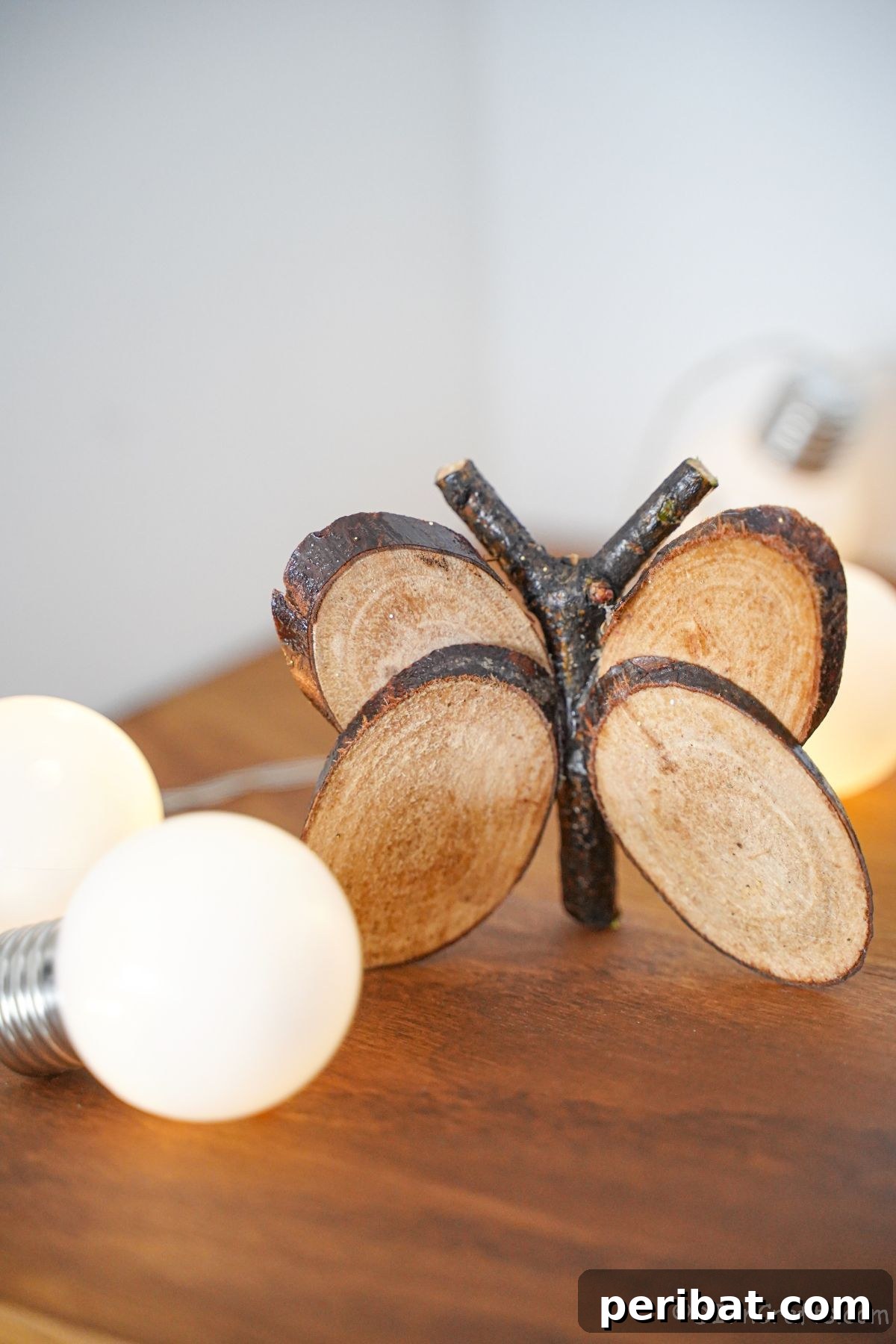A close-up of the rustic wood slice butterfly, gently illuminated by soft white fairy lights on a table, creating a cozy and magical ambiance