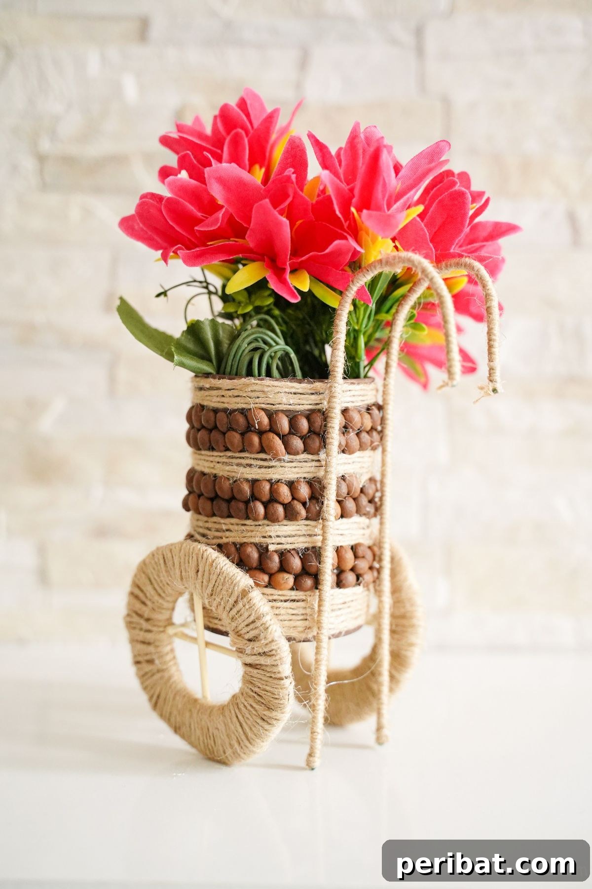 Rustic tin can vase holding pink flowers by white brick wall, adorned with coffee beans and twine.