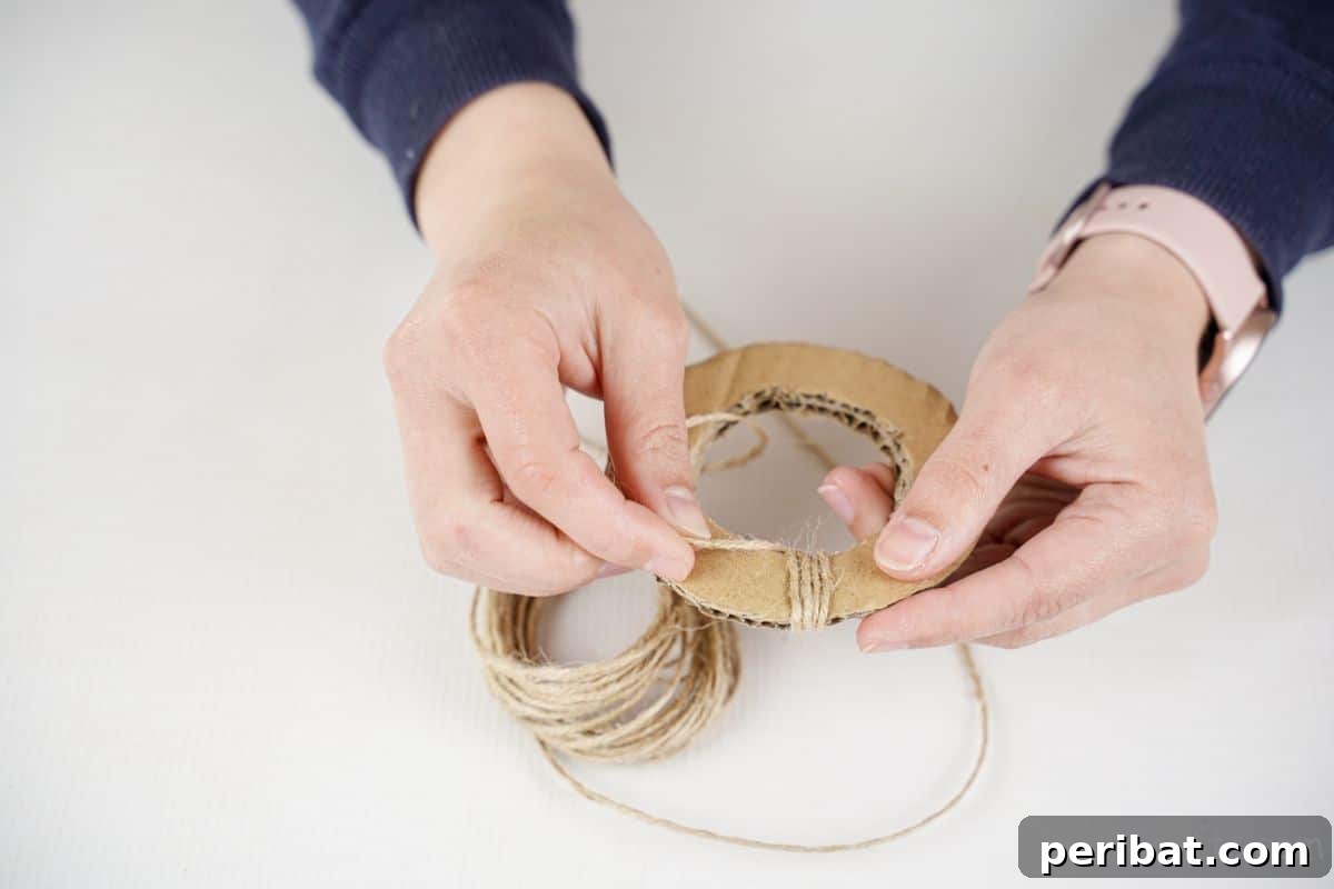 Hand meticulously wrapping natural twine around a cardboard circle, creating a rustic wheel.