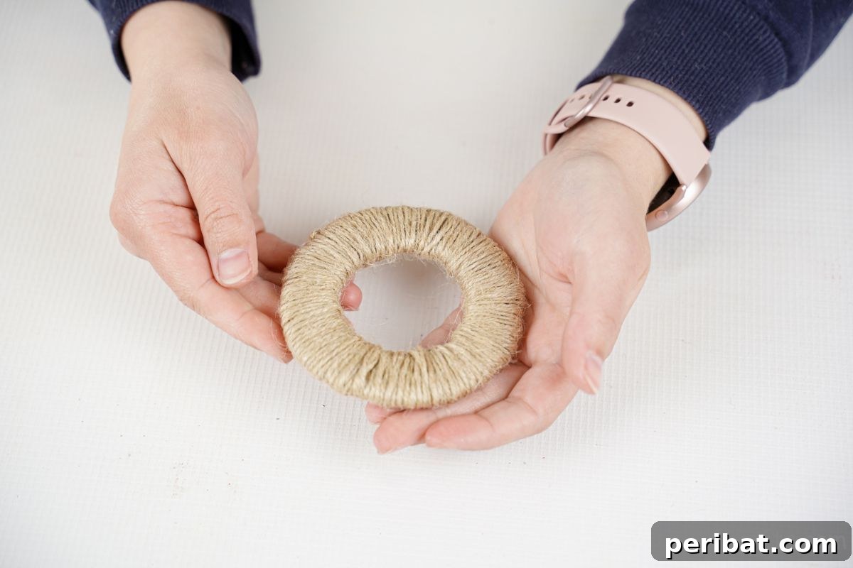 Close-up of a hand holding a finished twine-wrapped cardboard circle, a perfect rustic wheel.