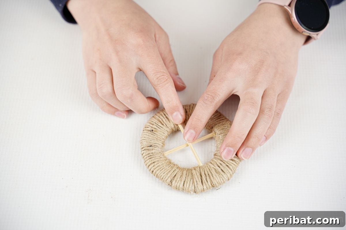 Two dowel pieces being glued in a criss-cross pattern onto a twine-wrapped wheel.