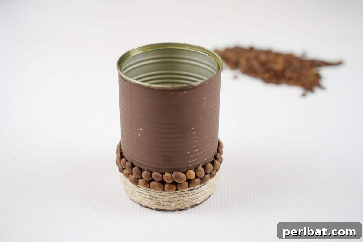 Brown tin can adorned with a section of coffee beans and twine, sitting on a white table.