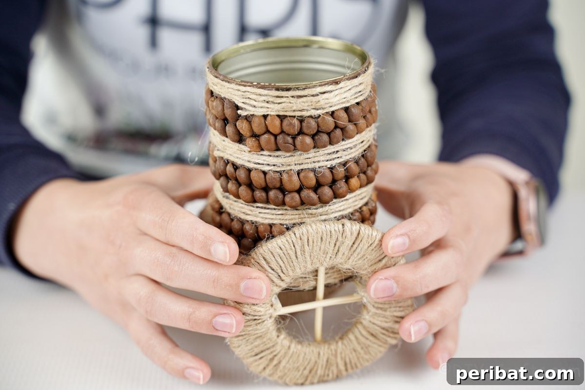 Holding a fully decorated tin can over the cardboard wheels, preparing to glue them together.